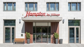 L’entrée d’un hôtel, avec une porte en verre transparent, un banc et des plantes en pot.