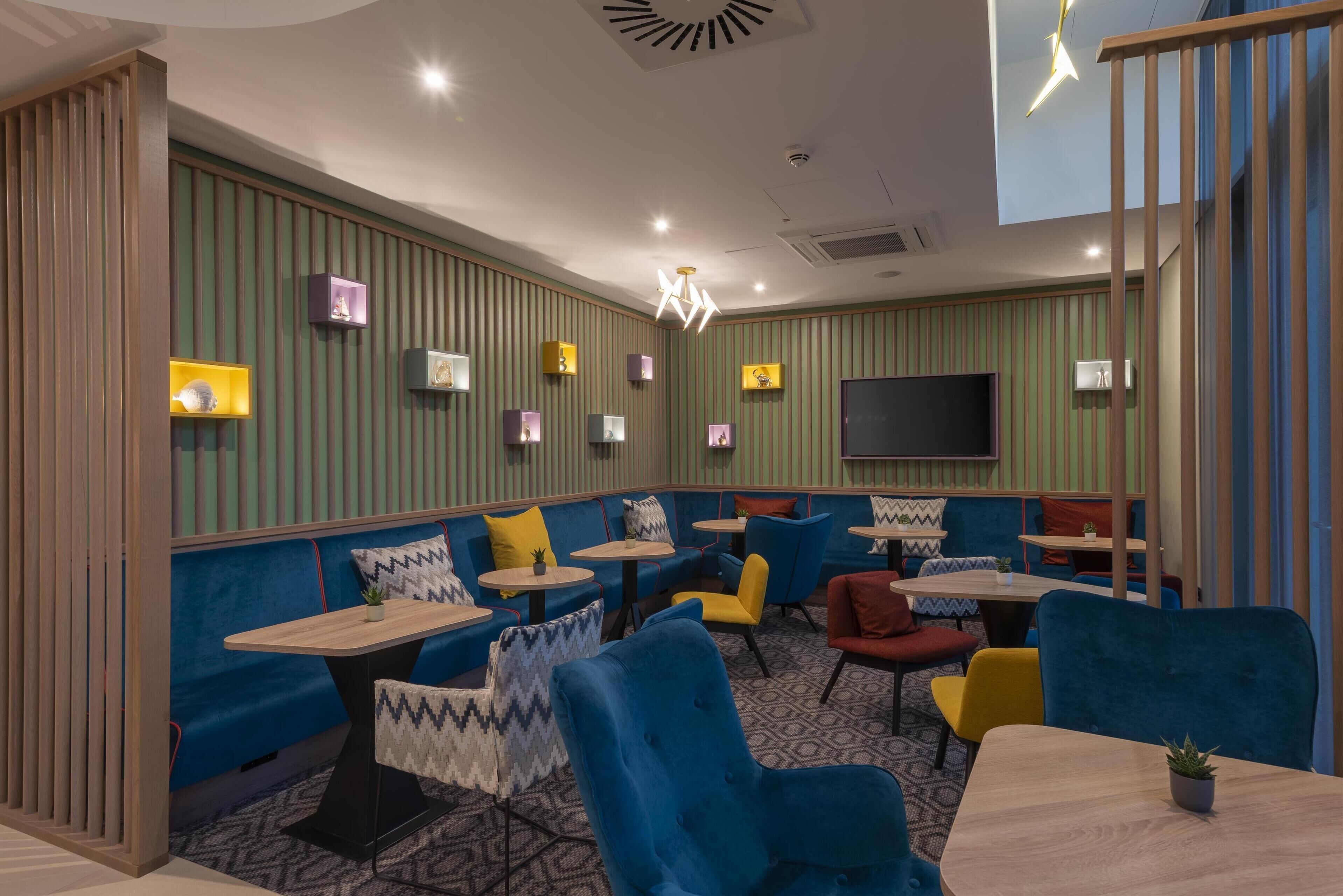 Ein modernes Restaurant mit Sitzecken, runden Tischen und einem Flachbildfernseher an der Wand.