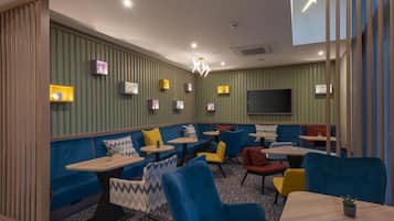 Un restaurante moderno con cabinas, mesas redondas y un televisor de pantalla plana en la pared.