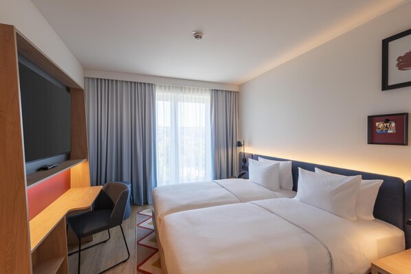 Habitación de hotel con dos camas, un escritorio, una silla, un televisor y una ventana con cortinas.