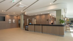 Un espace d’accueil moderne comprenant un comptoir, une plante en pot et un coin salon avec des chaises et une table.