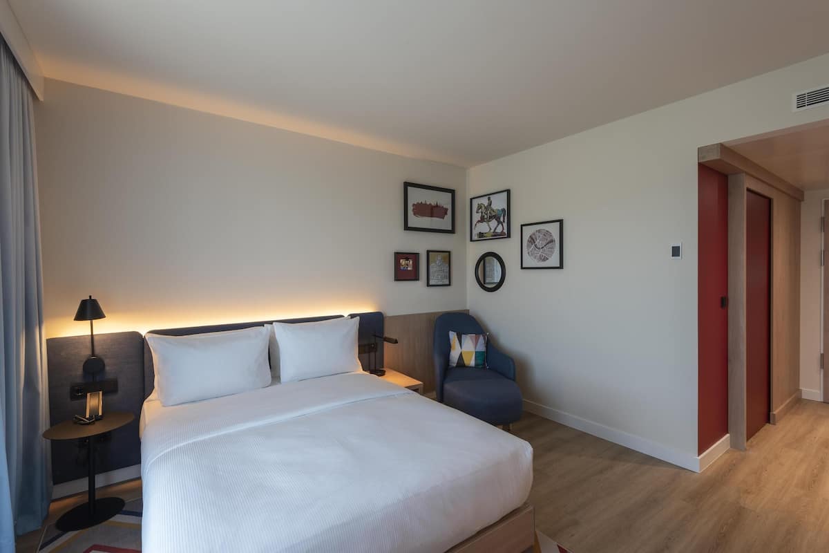 Une chambre d’hôtel avec un grand lit, des tables de chevet, une chaise et des œuvres d’art accrochées au mur.