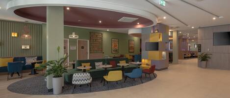 A modern lobby with a curved seating area, a reception desk, and a large screen.