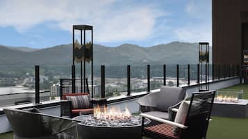 Una terraza en la azotea con mobiliario exterior, una chimenea y vistas a la ciudad y las montañas.
