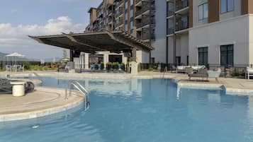 Una piscina con zona cubierta, sillas de descanso y vista a una montaña al fondo.