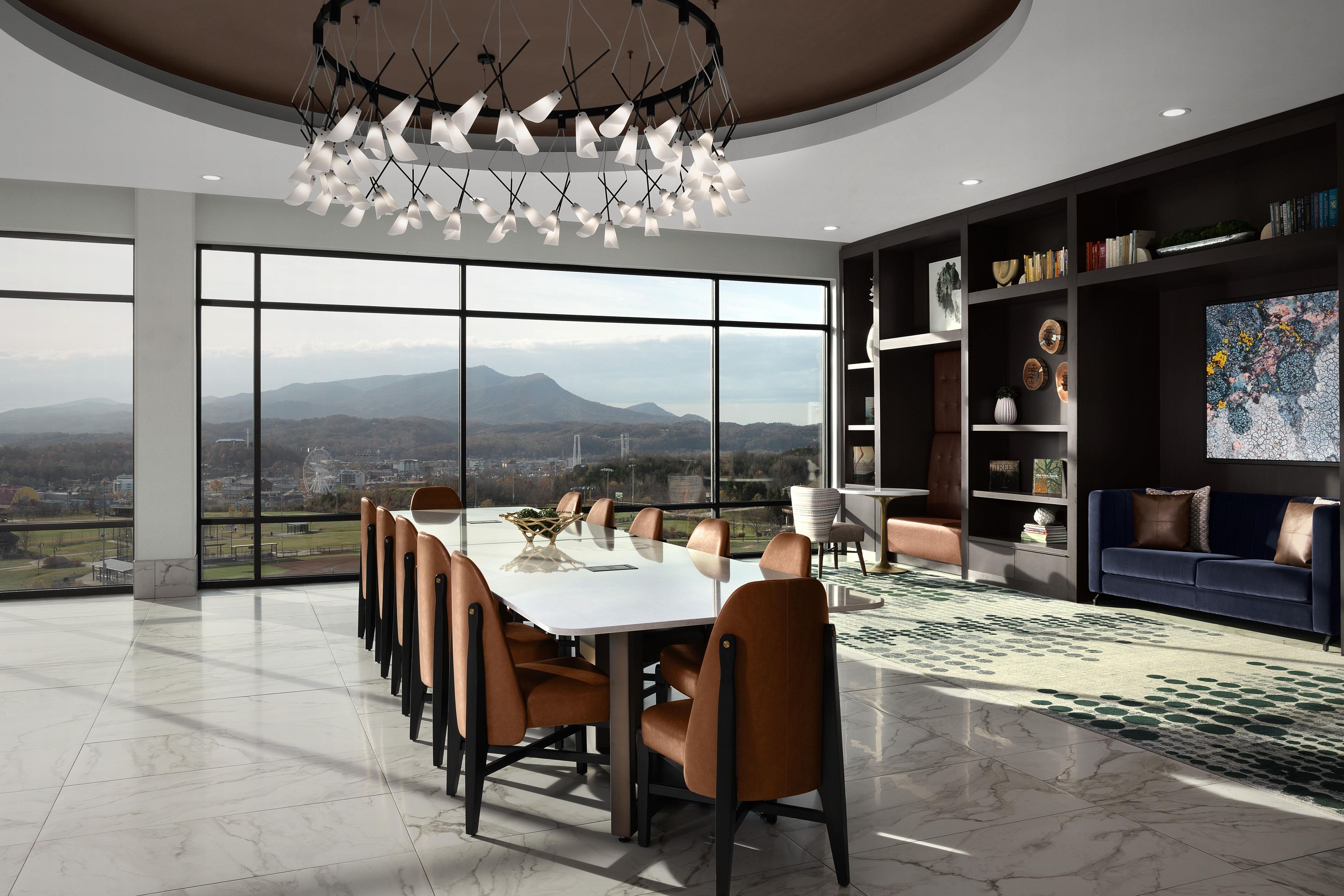 Un interior moderno con una gran mesa de comedor, asientos cómodos, una estantería y vistas al exterior.