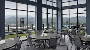 A restaurant with large windows offering a view of a city and mountains. Tables are arranged for dining.