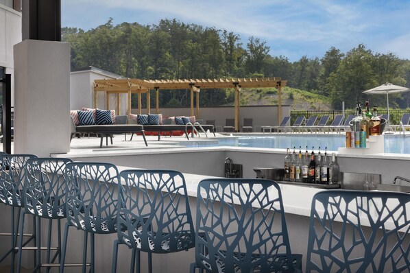 Un espace aménagé au bord de la piscine, avec des sièges de bar, des chaises longues et une pergola.