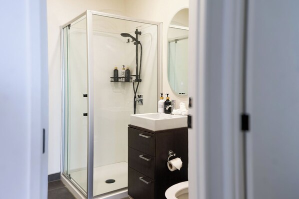 Un baño moderno con cabina de ducha de vidrio, tocador de madera oscura y lavabo blanco.