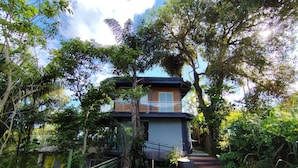 A modern two-story house with a balcony, surrounded by lush greenery and a well-maintained lawn. - House with lounge balcony and panoramic view in Vargem Grande, (Vargem Grande Rio de Janeiro)