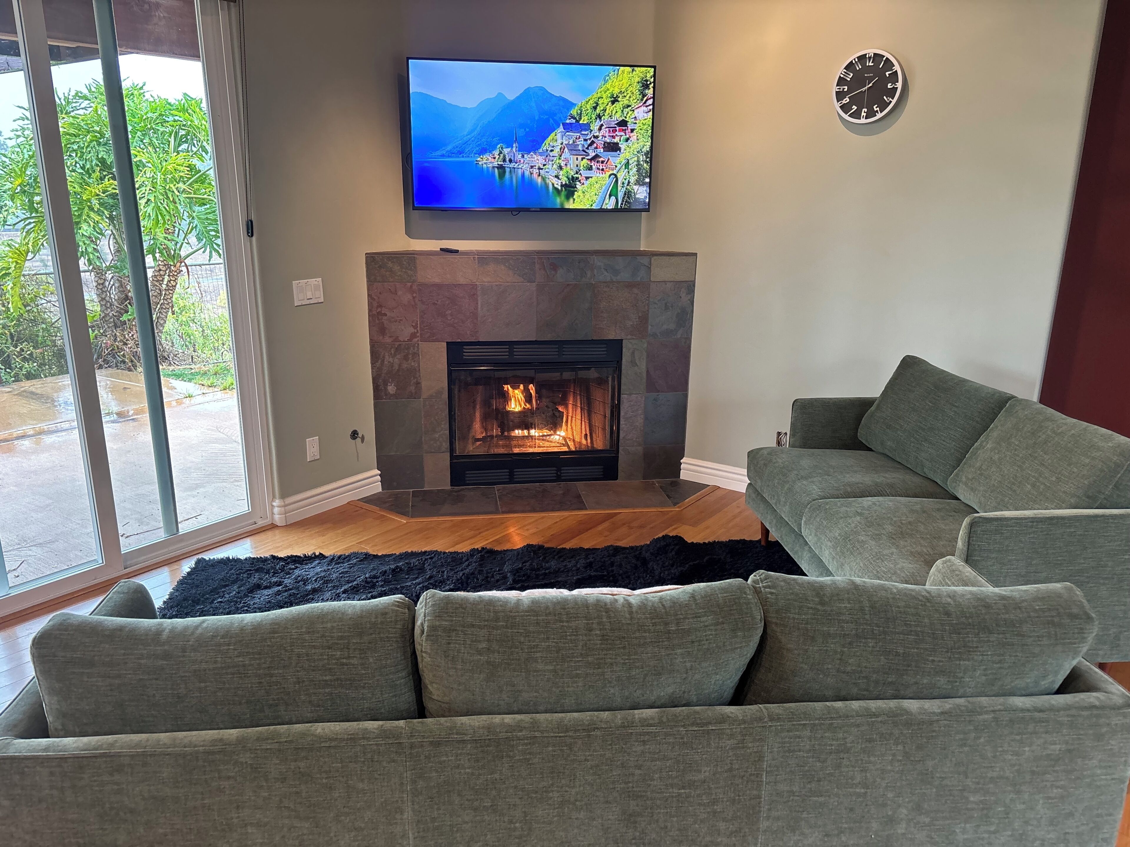 A living room with a stone fireplace, a television mounted above it, and a grey sofa.