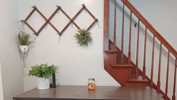 A dining area with a wooden table, two stools, a hanging plant, and a staircase.