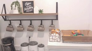 A kitchen with a coffee maker, sugar and tea containers, a microwave, and a shelf with mugs and a sign.