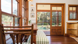 Comedor de madera con banco, una mesa y vistas a una piscina y árboles a través de un ventanal.