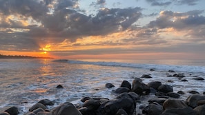 A beach with large rocks in the foreground and a sunset over the ocean.