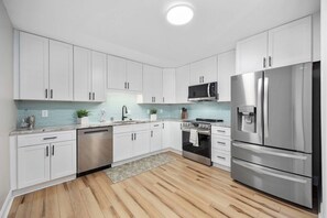 A modern kitchen with white cabinets, stainless steel appliances, and a tiled backsplash.