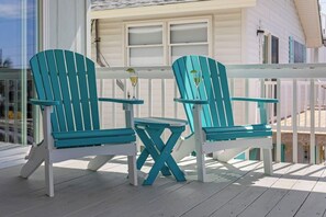 Two turquoise Adirondack chairs with a small table on a wooden deck.