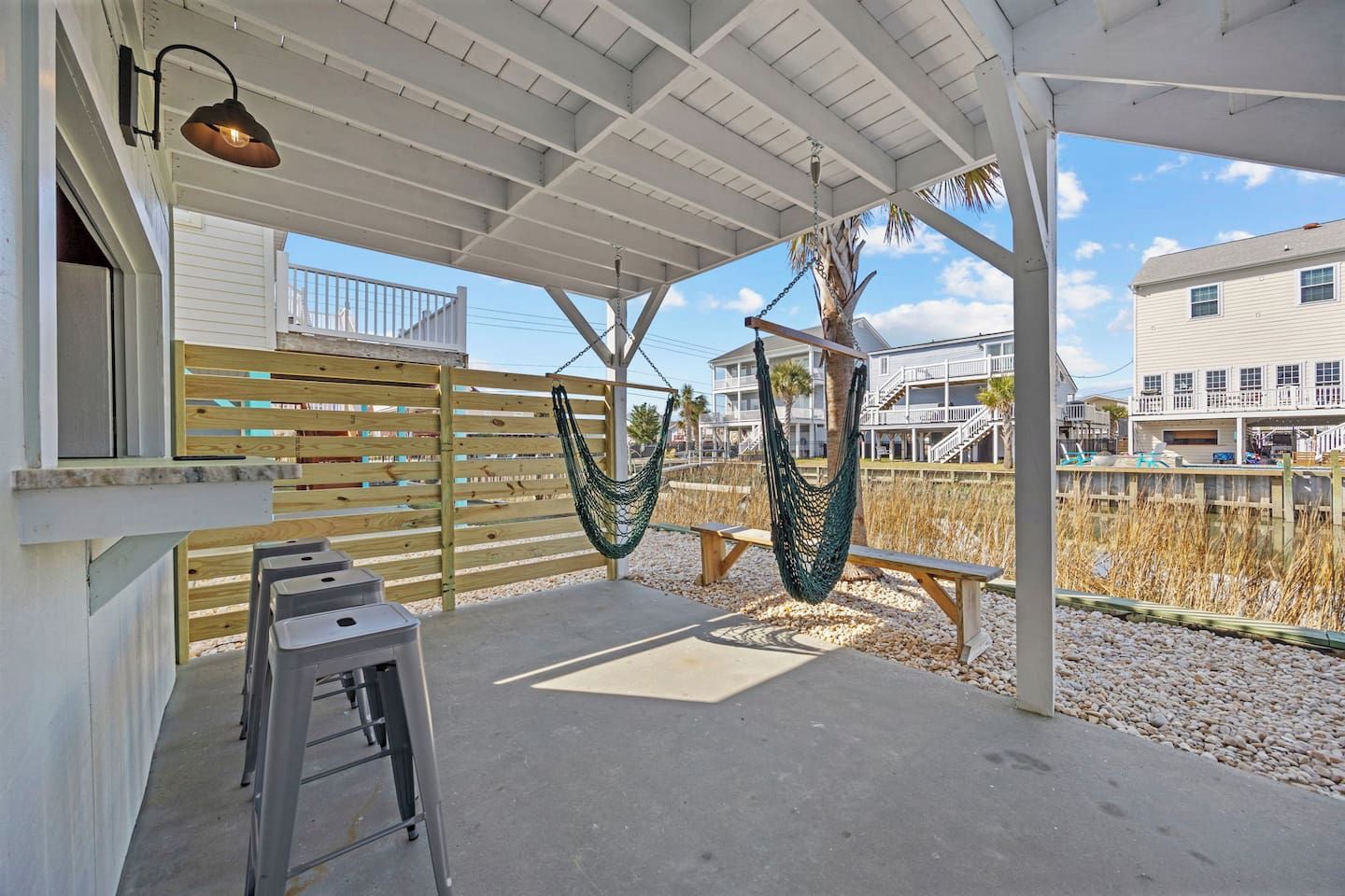 A covered outdoor area with a wooden fence, two hammocks, a bench, and a concrete floor.