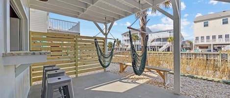 A covered outdoor area with a wooden fence, two hammocks, a bench, and a concrete floor.