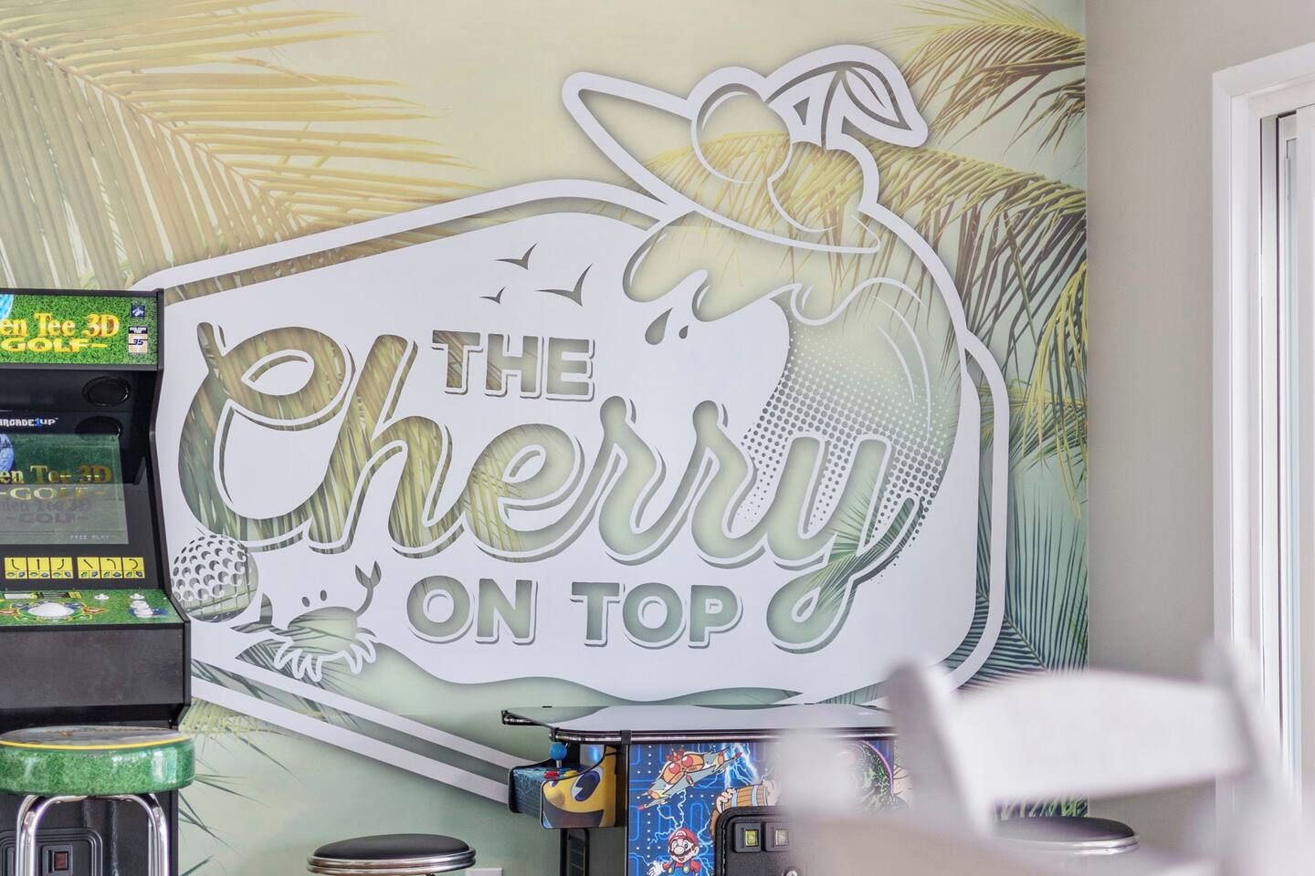 A wall with a sign that reads 'THE Cherry ON TOP' and a 3D golf game machine.