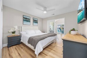 A bedroom with a bed, a nightstand, a dresser, a ceiling fan, and a view of the outside.