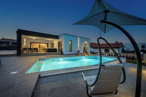 Relax by the rectangular pool surrounded by a paved deck and lounge chair.