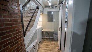 A narrow hallway with a wooden floor, a white ironing board, and a laundry basket.
