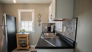 A modern kitchen with a stainless steel refrigerator, a wooden cart, a double sink, and a window with a view.