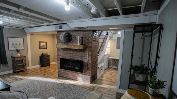 A spacious living room with a brick fireplace, wooden flooring, and a staircase leading to an upper level.