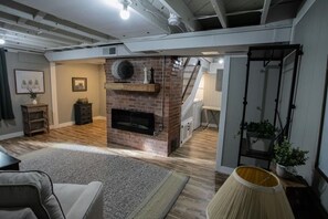 Un vaste salon doté d’une cheminée en briques, de planchers en bois et d’un escalier menant à l’étage supérieur.