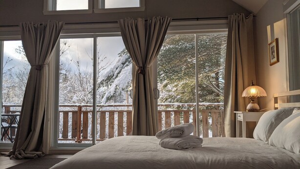 Een slaapkamer met een groot bed, een nachtkastje met een lamp en uitzicht op een besneeuwd terras.
