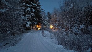 Een besneeuwde weg die naar een huis leidt, met een verlichte veranda.