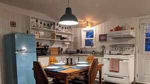 Een keuken met een blauwe koelkast, een witte kookplaat, een houten eettafel en stoelen.