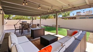 An outdoor patio with a covered seating area, a dining table, and a grill.