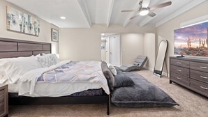 A bedroom with a bed, a ceiling fan, a dresser, and a large TV on the wall.