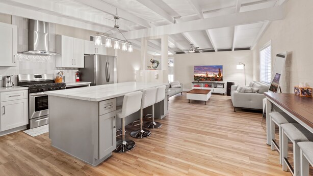 A modern kitchen with a central island, bar stools, and a dining area with a wooden table and benches.