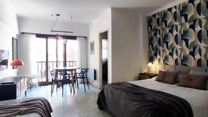 Une chambre d’hôtel avec un lit, un bureau, une chaise, une table et un mur décoré d’un motif.