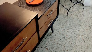 Une commode de style vintage, dotée de tiroirs, sur laquelle est posée une lampe rouge.