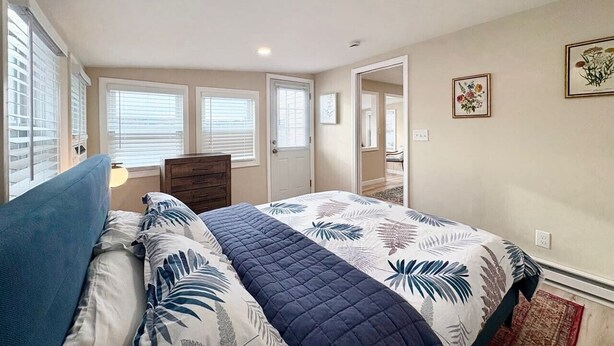 Une chambre à coucher avec un lit, une commode, une porte et une fenêtre avec des stores.