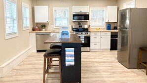 Une cuisine moderne dotée d’un îlot central, d’appareils électroménagers en acier inoxydable et d’un plancher en bois clair et épuré.
