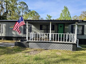 A small, single-story house with a porch, a green door, and an American flag. - Emerald Cottage Oasis (Jacksonville)