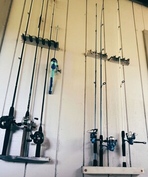 A wall-mounted fishing rod rack with multiple fishing rods and reels. - Emerald Cottage Oasis (Jacksonville)