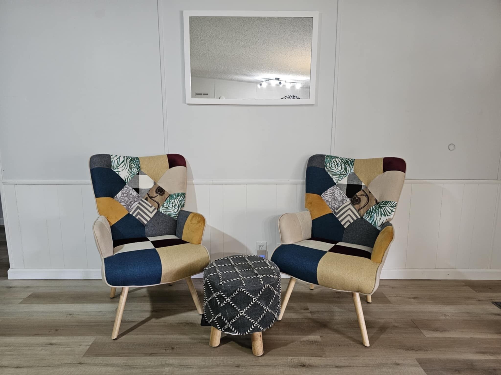 Zwei Sessel mit Patchwork-Muster, ein kleiner Hocker und ein Spiegel an der Wand.