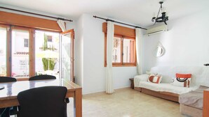 A room with a dining table, chairs, a sofa, and a window with curtains. - Salinas - Studio (Calpe)