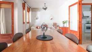 A dining area with a wooden table, chairs, a chandelier, and a kitchen visible through an open door. - Salinas - Studio (Calpe)