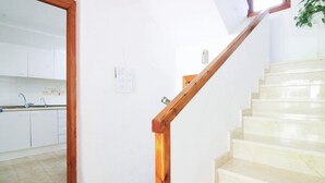 A staircase with wooden handrails leading to a kitchen area with white cabinets and a tiled floor. - Salinas - Studio (Calpe)