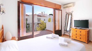 A bedroom with a bed, a television, a wooden dresser, and a balcony with a view of buildings and plants. - Salinas - Studio (Calpe)