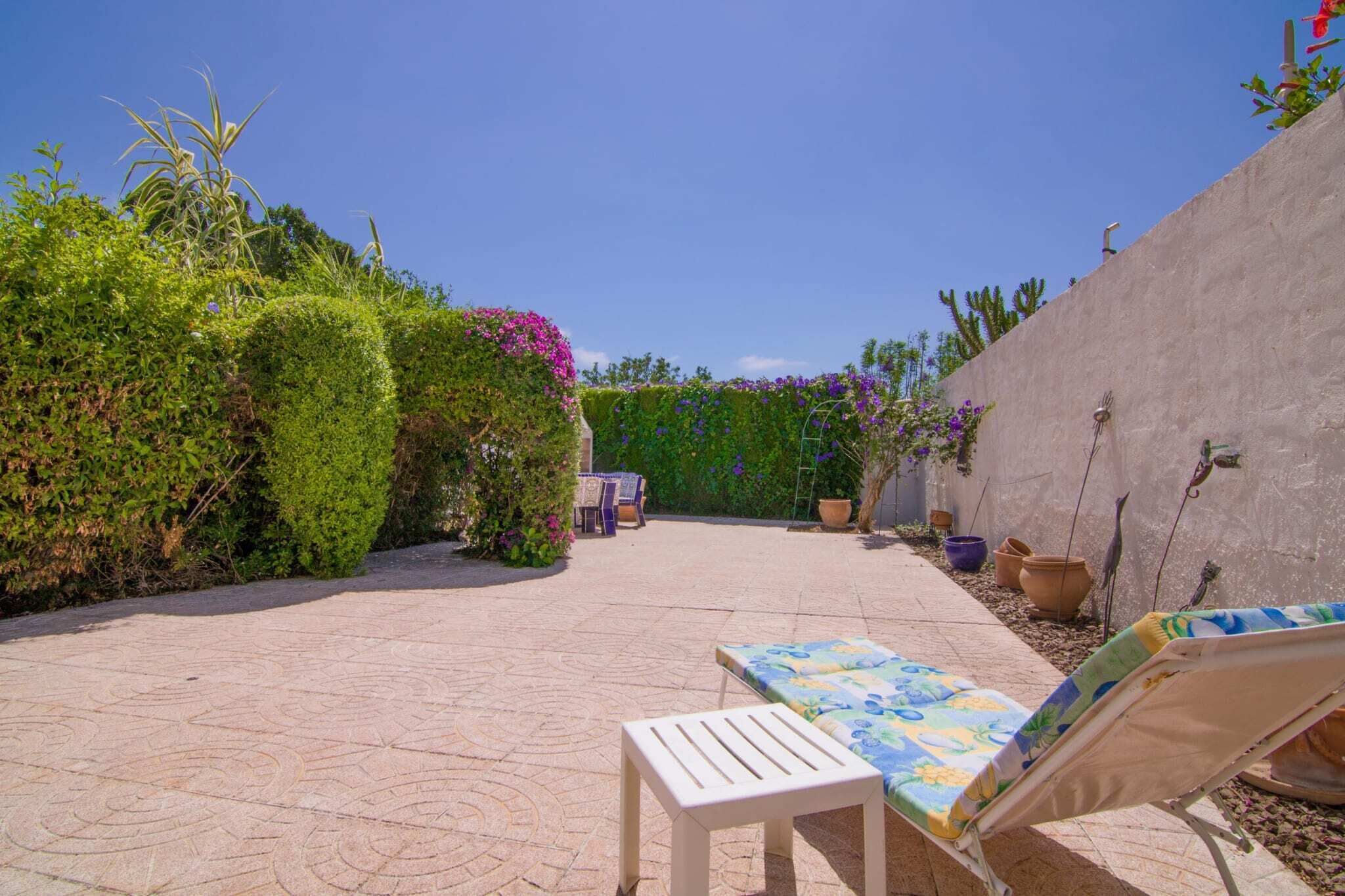 A patio with two lounge chairs, a table, and potted plants.