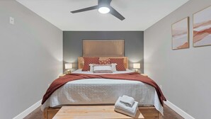 A bedroom with a bed, bedside lamps, a ceiling fan, and a small table with a towel.