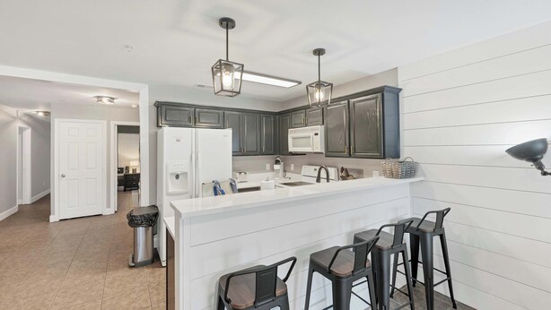 A modern kitchen with dark cabinets, a white countertop, and bar stools.